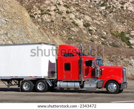 Red tractor truck with white trailer on mountain road parking lot with rocky cliff