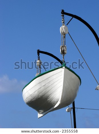 White wood emergency escape rescue life boat hanging from davits over a ship deck