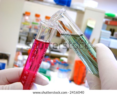 Scientist hands holding a laboratory glass scientific cylinder filled with green liquid and mixing it into a graduated test tube full of chemical solution for an experiment in a science research lab