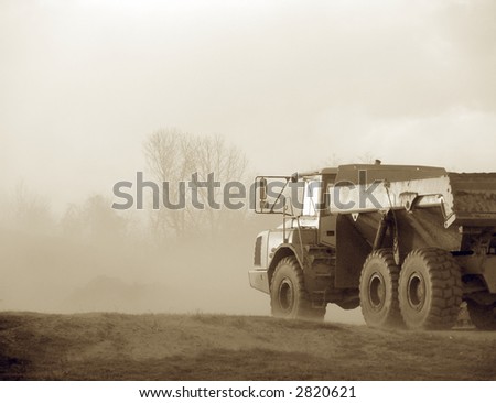 Articulated hauler truck driving in dust cloud on road work construction site