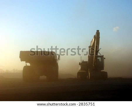 Heavy duty dirt hauler work truck and hydraulic excavator in dust storm on construction site at sunset
