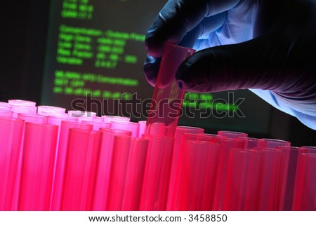 Scientist hand holding a laboratory pink plastic test tube before a scientific computer monitor with results data for an experiment in a science research lab