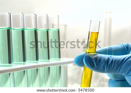 Scientist hand holding a laboratory glass test tube filled with yellow liquid near a rack of chemistry tubes for an experiment in a science research lab