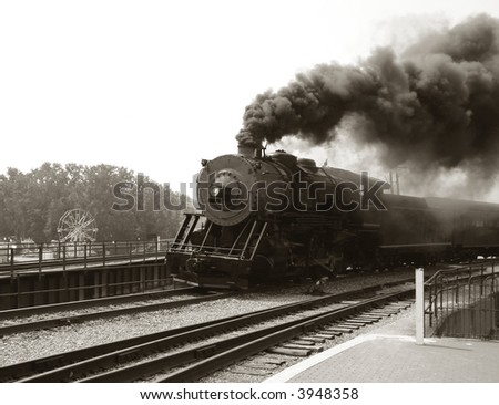 Vintage steam engine locomotive speeding on railroad tracks curve and blowing heavy black smoke while pulling an antique passenger train in nostalgic sepia