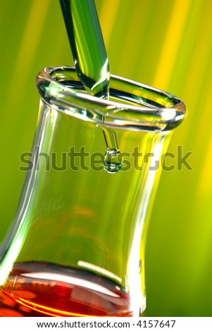 Laboratory pipette with drop of green liquid inside conical glass Erlenmeyer flask filled with red liquid for an experiment in a science research lab