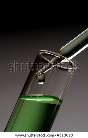 Laboratory pipette with drop of liquid over test tube filled with green liquid chemical for an experiment in a science research lab