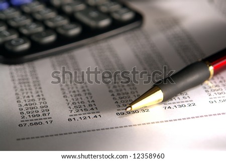 Ballpoint pen and calculator over financial statement spreadsheet with Dollar numbers in dramatic light
