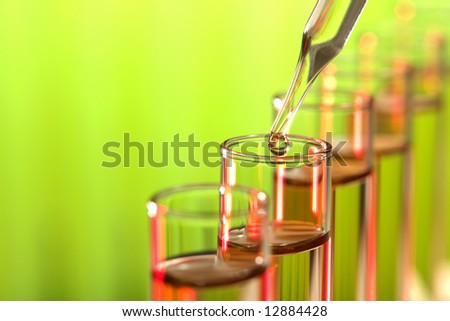 Laboratory glass pipette with drop of liquid over test tubes for an experiment in a science research lab