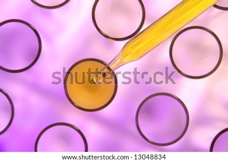Laboratory glass pipette filled with yellow liquid over test tubes viewed from above for an experiment in a science research lab