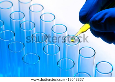 Scientist hand holding a laboratory glass pipette with drop of yellow liquid over test tubes for an experiment in a science research lab