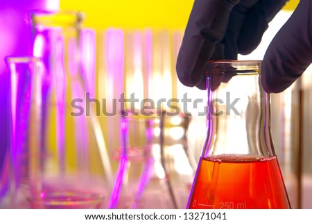 Scientist hand holding a laboratory glass conical Erlenmeyer flask filled with red liquid for an experiment in a science research lab