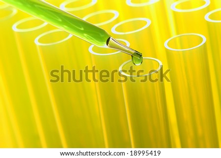 Laboratory pipette with drop of green liquid over yellow plastic test tubes for an experiment in a science research lab