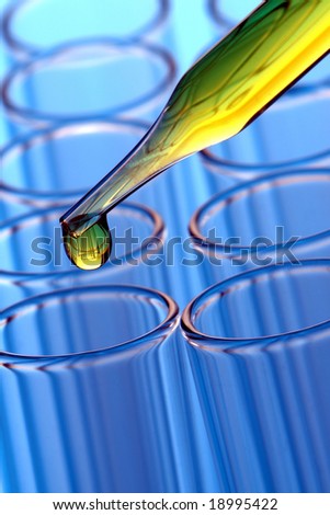 Laboratory pipette with drop of yellow liquid over test tubes for an experiment in a science research lab