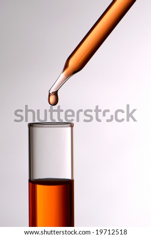 Laboratory pipette with drop of red liquid above test tube for an experiment in a science research lab