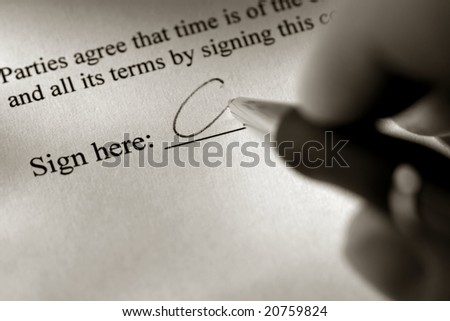 Fingers holding an ink pen and signing a contract document on the sign here signature line