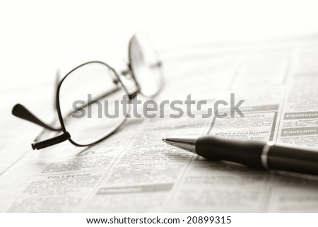 Ballpoint pen and reading glasses on newspaper jobs and help wanted employment classifieds ads section for an unemployment recovery job search
