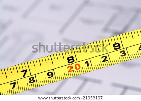 Self retracting construction tape measure with inch and centimeter markings over house builder floor plan