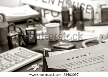 Home sale resale contract in agent presentation binder with real estate title documents over busy Realtor desk in realty brokerage sales office with tools of the trade and business supplies