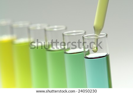 Laboratory pipette with drop of yellow liquid over glass test tubes for an experiment in a science research lab