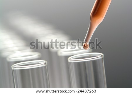 Laboratory pipette with drop of red liquid over empty chemistry test tubes for an experiment in a science research lab