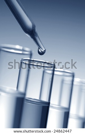 Laboratory pipette with drop of liquid over glass test tubes for an experiment in a science research lab