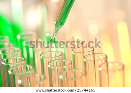 Laboratory pipette with drop of green liquid over glass test tubes for an experiment in a science research lab