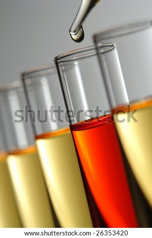 Laboratory pipette with drop of clear liquid over glass test tubes filled with red and yellow chemical solution for an experiment in a science research lab