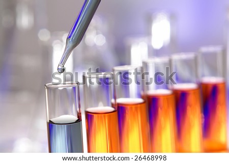 Laboratory pipette with drop of blue liquid over test tubes filled with orange chemical solution for an experiment in a science research lab