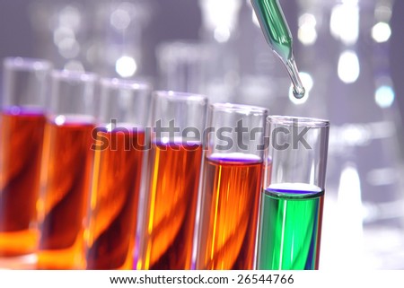 Laboratory pipette with drop of green liquid over test tubes filled with orange chemical solution for an experiment in a science research lab