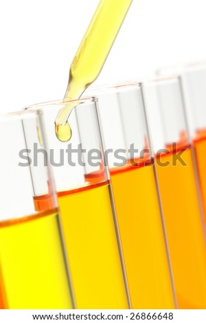 Laboratory pipette with drop of yellow liquid over glass test tubes filled with orange chemical solution for an experiment in a science research lab