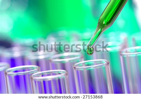 Laboratory pipette with drop of green liquid over glass test tubes for an experiment in a science research lab