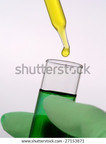 Laboratory pipette with drop of yellow liquid over glass test tube filled with green chemical solution in scientist hand for an experiment in a science research lab