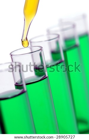 Laboratory pipette with drop of yellow liquid over glass test tubes filled with green chemical solution for an experiment in a science research lab
