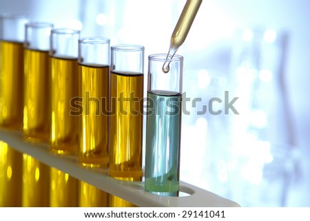 Laboratory pipette with drop of yellow liquid over glass test tubes filled with blue chemical solution for an experiment in a science research lab