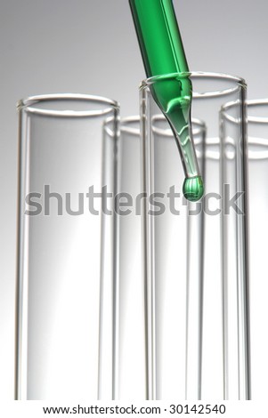 Laboratory pipette with drop of green liquid inside empty glass test tubes for an experiment in a science research lab