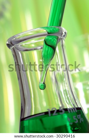 Laboratory pipette with drop of green liquid inside laboratory conical Erlenmeyer flask for an experiment in a science research lab