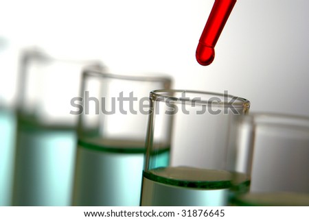 Laboratory pipette with drop of red liquid over glass test tubes filled with green chemical solution for an experiment in a science research lab