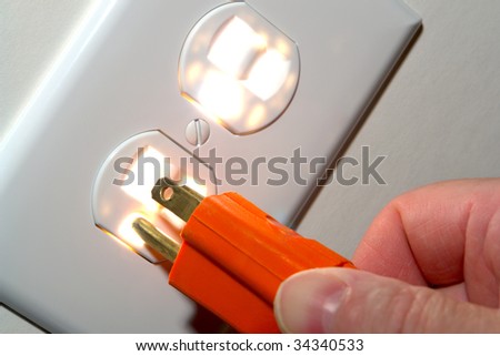 Fingers inserting a power cord plug into a glowing North American standard 110 volt electric wall outlet receptacle