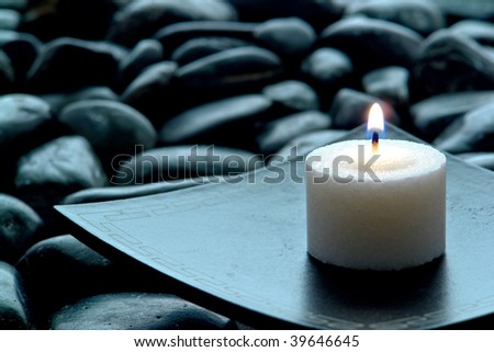 Meditation candle burning on an Asian inspired plate over bed of black stones in an evening religious ceremony