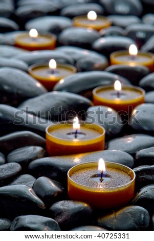 Meditation candles burning with a soft glow flame on a bed of black polished stones in a Zen inspired path for a spiritual and meditative Eastern influenced religious session