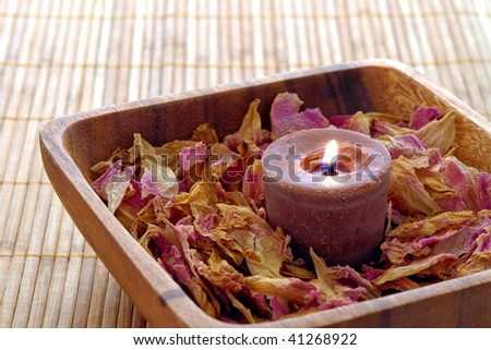 Aromatherapy organic candle burning on a bed of flower petals in a wood dish on a bamboo mat in a spa
