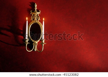 Antique gold gilded wall candelabra mirror sconce with burning wax candles on a red wall in a historic home