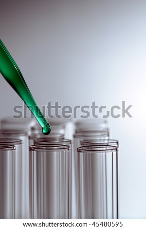 Laboratory pipette with drop of green liquid above empty chemical test tubes for a chemistry experiment in a science research lab
