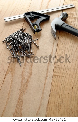 Pile of common nails and steel claw carpentry hammer with builder square on oak wood planks bench at a house construction work site