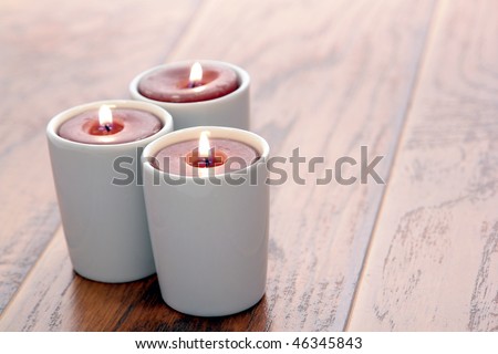 Aromatherapy scented candles burning in decorative ceramic candle holders on wood furniture