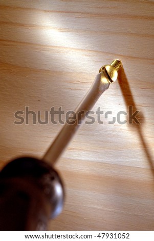 Slotted screwdriver driving a brass screw into a wood board