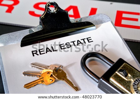 Paperwork with the words real estate on a clipboard with set of house keys and lockbox