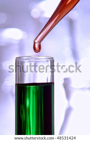Laboratory pipette with drop of red liquid above a test tube filled with green chemical solution for an experiment in a science research lab