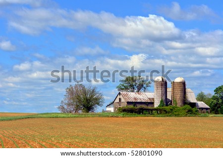 Old farm barn building with silos and recently planted agricultural field