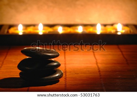 Polished black stones Zen inspiration cairn with row of soft burning candles on bamboo mat for a soft relaxation and quiet meditation